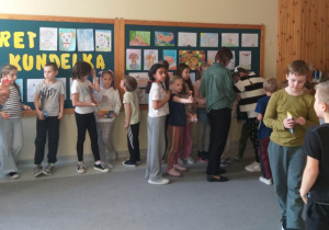 Na zdjęciu widać dzieci stojących przed dużą tablicą na ścianie. Tablica jest ozdobiona napisem z żółtych liter oraz wieloma kolorowymi rysunkami przedstawiającymi psy wykonanymi przez dzieci.