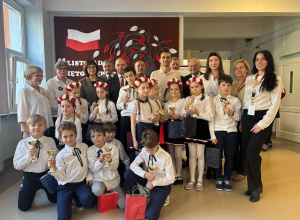 Na zdjęciu widać grupę dzieci i dorosłych pozujących wspólnie w szkolnym korytarzu.