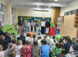 Na zdjęciu widać dzieci siedzące na podłodze i oglądające przedstawienia.