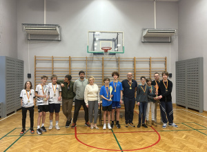 Na zdjęciu widać grupę młodych zawodników oraz dorosłych stojących razem w sali gimnastycznej, najprawdopodobniej podczas ceremonii zakończenia turnieju tenisa stołowego.