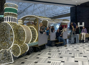 Na zdjęciu widać grupę dzieci oraz kilka osób dorosłych pozujących przy dużej, dekoracyjnej instalacji w kształcie świątecznego pociągu.