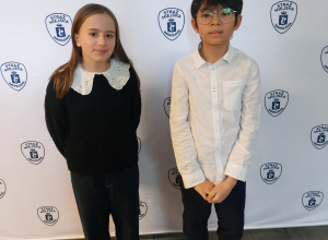 Uczeń i uczennica elegancko ubrani stoją na tle białej ściany z logo Straży Miejskiej.