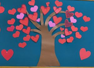 Na zdjęciu widać dekorację wykonaną z kolorowego papieru, umieszczoną na tablicy z turkusowym tłem. W centralnej części znajduje się duże, brązowe drzewo bez liści, wycięte z papieru.