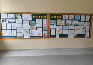 Na zdjęciu widać szkolną gazetkę ścienną umieszczoną w sali świetlicowej. Składa się ona z dwóch dużych, zielonych tablic w drewnianych ramach. Na środku, u góry, widnieje napis z żółtych liter: „DZIEŃ KOTA”. Tablice są wypełnione licznymi dziecięcymi rysunkami przedstawiającymi koty. Prace są wykonane głównie kredkami i ołówkiem. Niektóre rysunki przedstawiają pojedyncze koty, inne pokazują koty w różnych sceneriach – w domu, na dworze, wśród drzew czy przy misce. Całość znajduje się na jasnej ścianie, nad szarą podłogą.