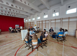 Uczniowie siedza przy stolikach.