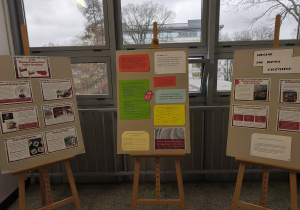 Korytarz szkolny. W tle okna. 3 stojaki z tablicami zawierającymi ciekawostki o języku polskim.