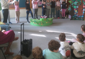 Dzieci wraz z nauczycielem stoją na scenie i trzymają w górze piktogramy, które ukazują, jak należy dbać o zdrowie psychiczne.