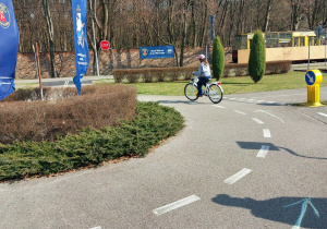 Miasteczko Ruchu Drogowego. Dziewczynka w kasku jeździ po specjalnie wyznaczonej trasie.