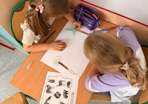 Dziewczynki siedzą przy sroliku i rysują zwierzęta lesne w swoim naturalnym środowisku.
