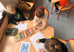 Troje uczniów siedzi przy stoliku i rysują zwierzęta, które żyją na Antarktydzie.